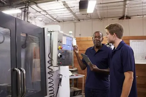 An instructor walking a trainee through a machine control panel on the shop floor